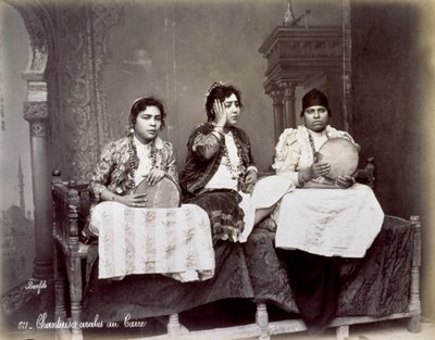 Portret trzech młodych arabskich śpiewaków w etnicznych strojach z długimi naszyjnikami. Pozują w studio, siedząc. Dwóch z nich trzyma tamburyn autorstwa Félix Bonfils