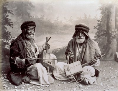 Portret dwóch arabskich muzyków w skromnych etnicznych strojach. Starsi panowie pozują w studio, siedząc na ziemi. Za nimi widać zalesiony krajobraz autorstwa Félix Bonfils