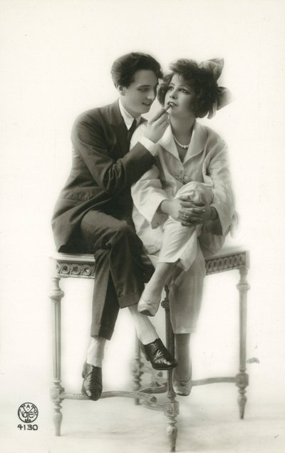 Androgyniczny mężczyzna w garniturze nakłada szminkę na usta dziewczyny w piżamie autorstwa French Photographer