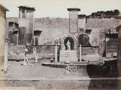 Częściowy widok na podwyższony ogród Domu Marka Lukrecjusza w Pompejach, ozdobiony marmurowymi posągami i hermami. W centrum fontanna z wnęką. W tle fragmenty malowideł ściennych autorstwa Giorgio Sommer