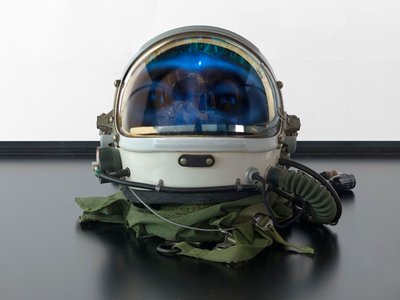 Alpha Omega, 2016 (szkło, ekran LCD, odtwarzacz multimedialny, replika czaszki, hełm kosmiczny, drewno) autorstwa Mat Collishaw