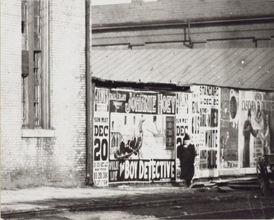 Mężczyzna przechodzi obok ściany z plakatami reklamowymi, w tym jeden dotyczący Johnnie Hoey The Boy Detective, granego w Havlin