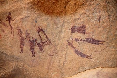 Sztuka naskalna, prehistoria: Malowidło naskalne przedstawiające grupę postaci i „guerba” (zewnętrzne) ma frędzle i bez frędzli w ozdobnym schronie, w masywie Uweinat w Sudanie. Okres od 8000 do 3000 lat pne. Fotografia autorstwa Unbekannt