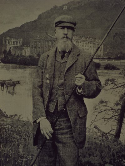 Portret studyjny ósmego księcia Devonshire w tweedach trzymającego wędkę przed wydrukowanym ekranem przedstawiającym Chatswortha autorstwa William M. Timlin