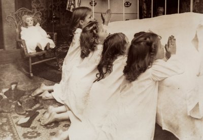 Cztery małe dziewczynki klęczące przy łóżku i odmawiające wieczorną modlitwę. autorstwa Unknown photographer