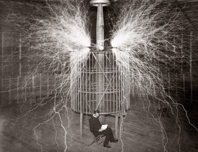 Nikola Tesla siedzący w swoim laboratorium w Colorado Springs ze swoim „nadajnikiem powiększającym” autorstwa Unknown photographer