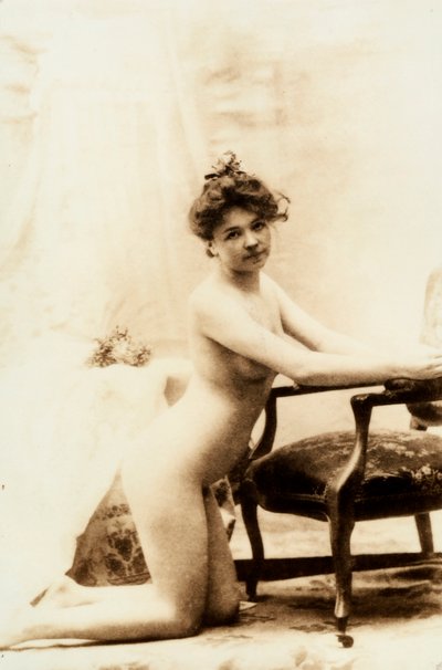 Nagi portret młodej kobiety klęczącej przed małym fotelem. autorstwa Unknown photographer