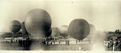 Balony na ogrzane powietrze na polu w South St. Louis gotowe do startu; jeden jest już na niebie w oddali autorstwa W.C. Persons