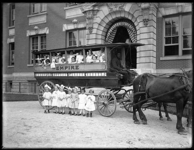 Małe dziewczynki pozują w i przed wozem ciągniętym przez konia, przed niezidentyfikowanym budynkiem, prawdopodobnie Roman Catholic Orphan Asylum, Kingsbridge, Bronx, ok. 1910 r. autorstwa William Davis Hassler