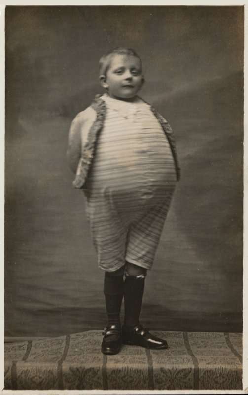Chłopiec w szkole, ubrany tak, by mieć bardzo duży brzuch (zdjęcie czarno-białe) autorstwa English Photographer