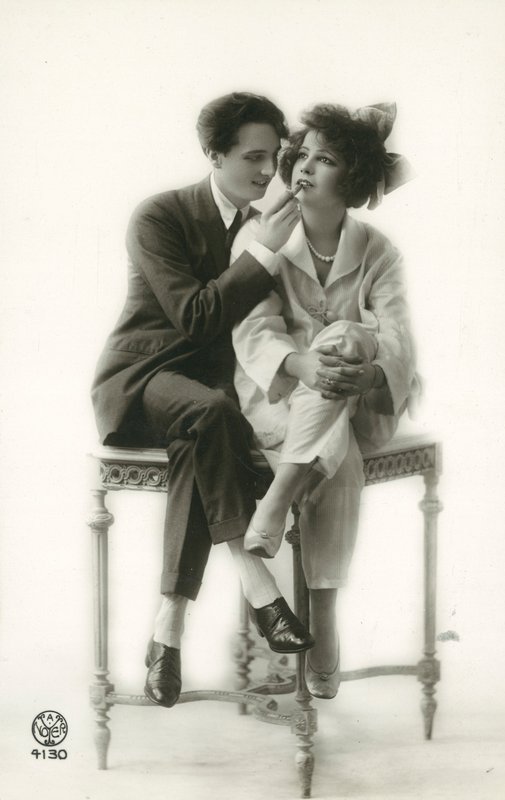Androgyniczny mężczyzna w garniturze nakłada szminkę na usta dziewczyny w piżamie autorstwa French Photographer