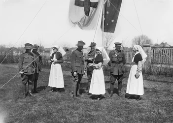 Grupa niezidentyfikowanych oficerów, pielęgniarek i mężczyzn z 3. Australian Casualty Clearing Station zebrała się pod masztem flagowym flagi Australii (Australian Blue Ensign) i Czerwonego Krzyża