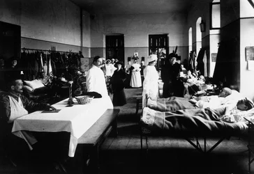 Zdobiony salon w szpitalu z rannymi, lekarzami, pielęgniarkami Czerwonego Krzyża i gośćmi (zdjęcie czarno-białe)