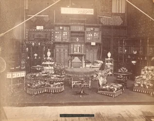 Wystawa S. Howard & Sons -- Gmach Główny, Kolekcja mebli, w tym krzesła tapicerowane, stoły, kominek, szafy i regały. Na ścianach dywany, a na stołach i półkach wazony