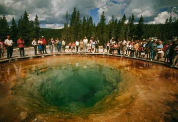 Odwiedzający park gromadzą się wokół niebieskozielonego basenu termalnego w kształcie kwiatu. Park Narodowy Yellowstone