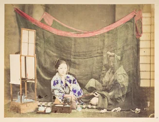 Japońska para w wolnym czasie, Studio tableau młodej Japonki, siedzącej z utrudnieniami parzenia herbaty, wręcza fajkę siedzącemu za nią mężczyźnie, osłoniętego lnianą moskitierą,   Fotograf: Nieznany  Kolekcja Lucasa: