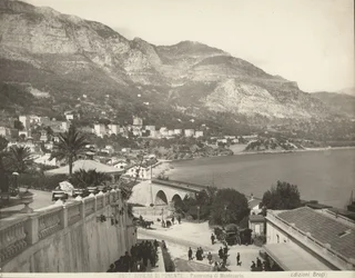 Panoramiczny widok na Montecarlo w Monako. Scena przedstawia różnych przechodniów; po lewej stronie w zbliżeniu marmurowa balustrada