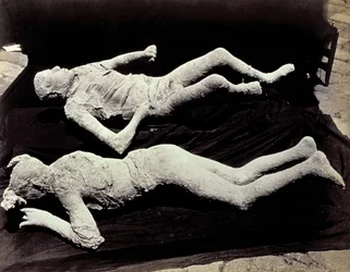 Dwa odlewy postaci ludzkich z wykopalisk w Pompejach. Eksponaty zostały umieszczone na czarnym materiale w celu ich sfotografowania