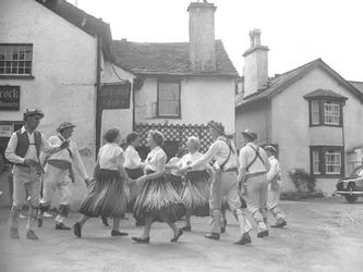 Mężczyźni i kobiety tańczący w Hawkshead z napisem "15 Century Café" z tyłu i licytatorami