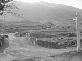 Widok drogi przechodzącej przez przełęcz Hardknott ze znakiem wskazującym kierunek Hardknott