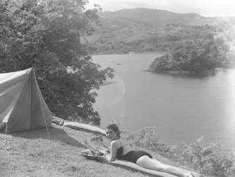 Widok młodej kobiety w kostiumie kąpielowym i leżącej na lilo, w tle jezioro