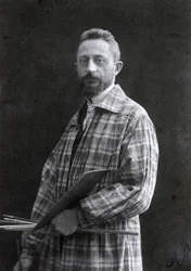Portret malarza Guido Spadoliniego w ujęciu trzy czwarte długości. Malarz ubrany jest w długą pelerynę, w lewej ręce trzyma pędzle i paletę, 26111901