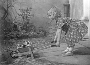 Mała dziewczynka bawi się taczką. Fotografia około 1931
