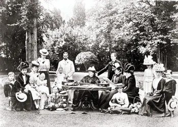 Członkowie brytyjskiej rodziny królewskiej, w tym król Jerzy V, król Edward VIII wokół królowej Wiktorii na przyjęciu w ogrodzie. Fotografia w latach 1895-1901.