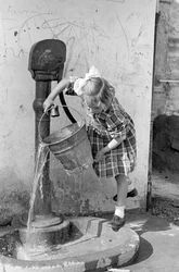Mała dziewczynka opróżniająca wiadro wody w fontannie z pompą, 9 maja 1939 r. (zdjęcie czarno-białe)