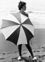 Kobieta z parasolem na plaży, ok. 1960 r. (zdjęcie czarno-białe)