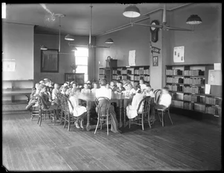 Dzieci słuchają kobiety w czytelni niezidentyfikowanej filii Queens Borough Public Library, ok. 1910