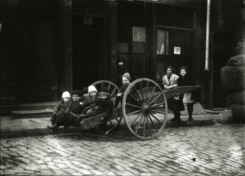 Grupa dzieci w wózku, z dziewczyną i kobietą stojącymi z tyłu, ok. 1910-21