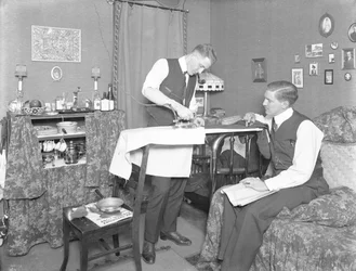 Niezidentyfikowany mężczyzna demonstrujący użycie żelazka elektrycznego, obserwowany przez innego mężczyznę, ok. 1913-14