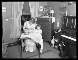 Niezidentyfikowana kobieta demonstrująca użycie żelazka elektrycznego, obserwowana przez małą dziewczynkę, ok. 1913-14